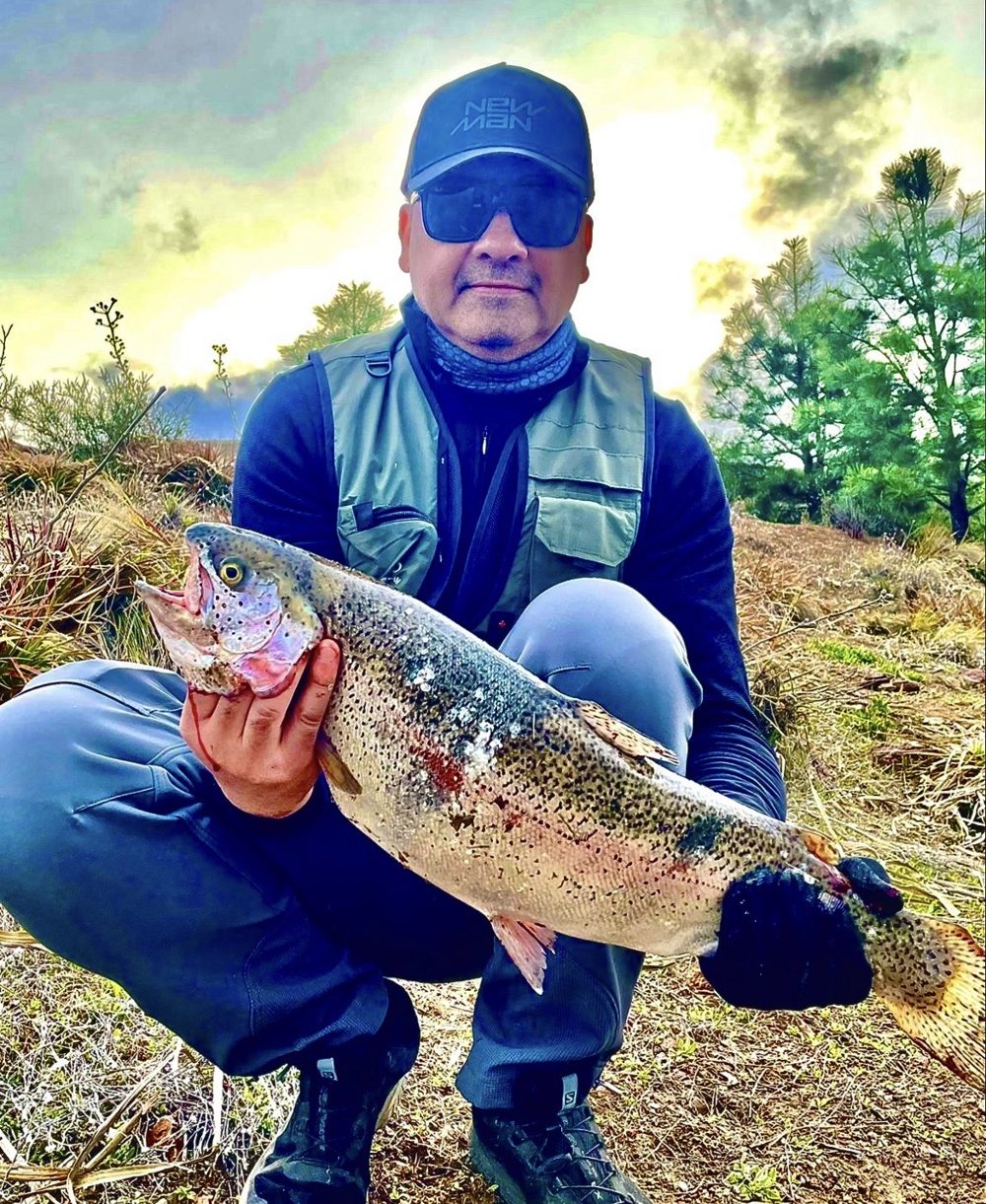 Angler crouching with a rainbow trout, at Las Trampas