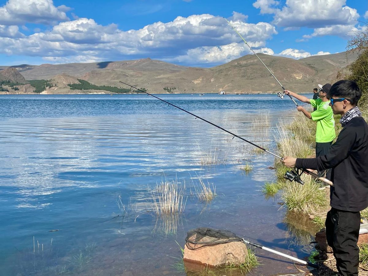 Three people spin fishing from the shore of the Alicurá Reservoir