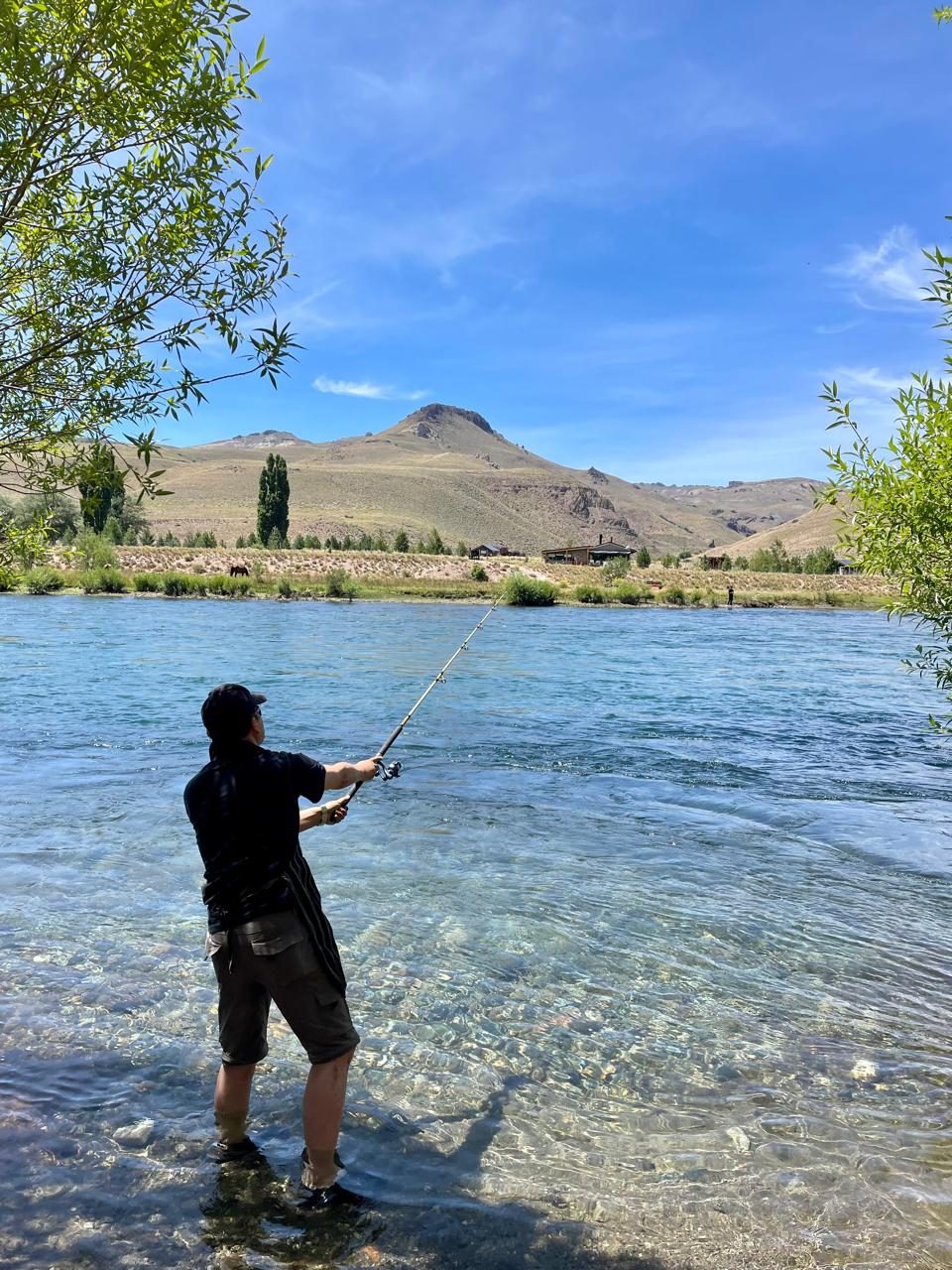 Angler casting a rod in a clear river, with steppe hills behind