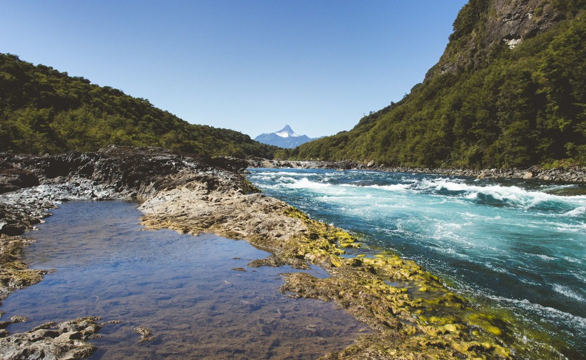Turquoise river between forested hills, with a snowy volcano behind